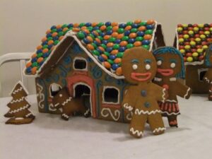 2 gingerbread figures beside a gingerbread house with roof covered in sweets, and a gingerbread dog and gingerbread Christmas tree; photo Wikimedia Commons