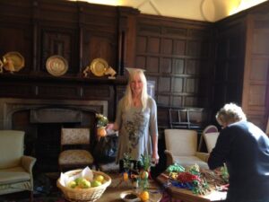 A photo of people in a wood-panelled room making traditional calennigs with fruit, sticks, candles and tinsel