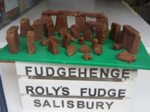 Model in a shop window of Stonehenge made out of fudge, on a green table top with a sign in front reading 'Fudgehenge. Roly's Fudge. Salisbury; photo Jeremy Harte