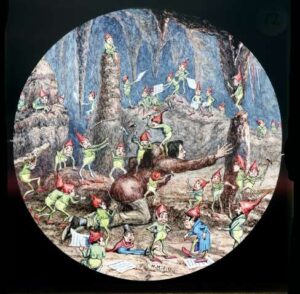 Magic lantern slide hand-painted by Henry Underhill of Oxford in 1892, from the set titled The Legend of Knockgrafton in The Folklore Society Archives. The image shows a man with a hunchback being attacked by a multitude of little fairies or elves clothed in green and with red pointed caps