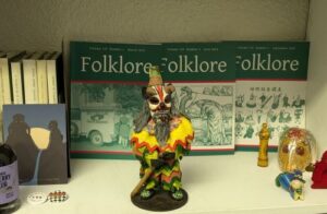 22cm painted plastic figure of a Brazilian 'Clown of 3 Kings' Day') wearing brightly coloured tatters, a horned and long-bearded mask, a conical hat and holding a stick 