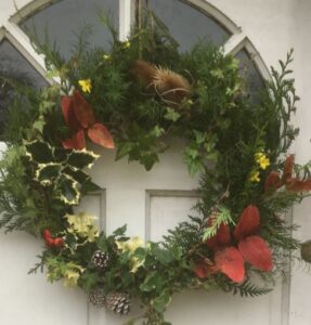 circular Christmas garland attached to a door, with variegated holly, ivy, cypress, teasels, and other foliage; photo C.Oates