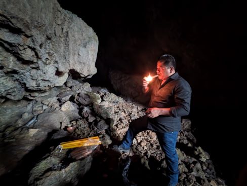 photo of a man standing on a mountain at night, lighting a cigar, with a pile of new candles at his feet,